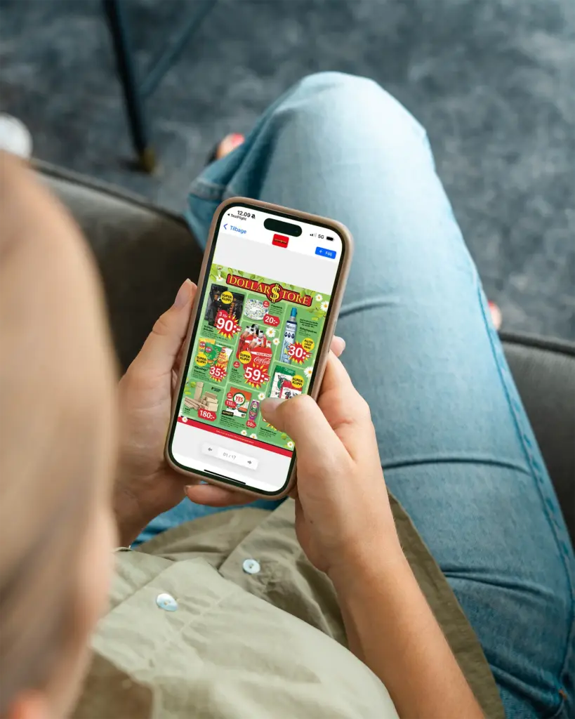 En person sitter med korsade ben och håller i en smartphone och tittar på en digital flyer som visar rabatter och reor på Dollar Store. Telefonens skärm visar olika färgglada prislappar.